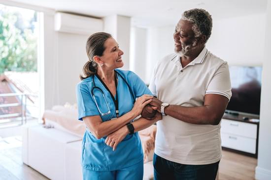A support worker steadying a smiling older man at his home
