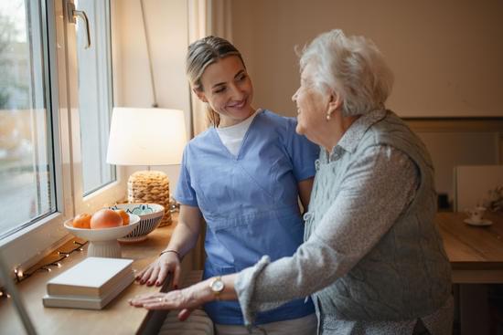 A caregiver and an older woman talking together in warm window light